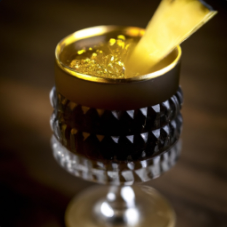 Black and Gold Touchdown cocktail in a glass with a gold rim and pineapple garnish.